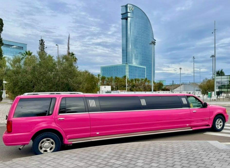 Limusina Hummer rosa frente al icónico Hotel W de Barcelona, símbolo de lujo y estilo para eventos, despedidas y celebraciones exclusivas.